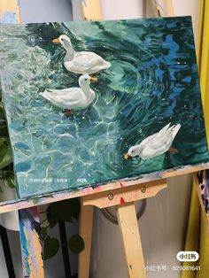 two white ducks are swimming in the water on an easel with paintbrushes