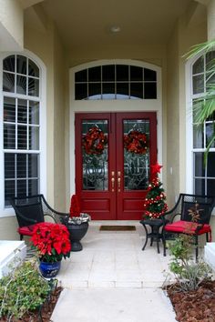 a red door with two chairs and christmas wreaths on the front entrance to a house