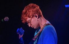 a young man with red hair and glasses playing the guitar in front of a microphone