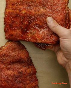 two pieces of meat sitting on top of a piece of parchment paper next to a person's hand