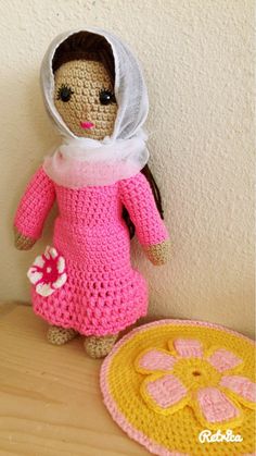 a crocheted doll with a pink dress and white bonnet sits next to a yellow plate