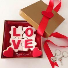 two heart shaped cookies in a box with red ribbon and keychain next to it