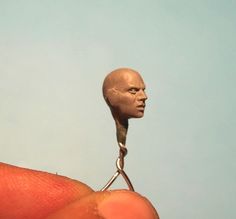 a person holding a miniature head on top of a pair of scissors