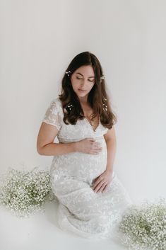 a pregnant woman sitting on the ground with her hands under her belly and flowers in front of her