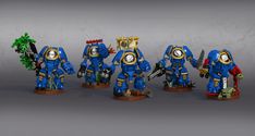 some blue and gold painted warhammers standing in front of a gray wall with trees