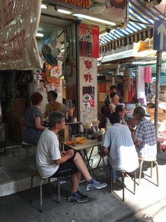 people are sitting at tables in front of a food stand on the side of the street