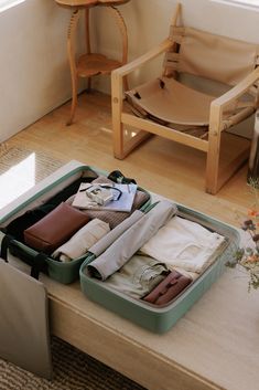 an open suitcase filled with clothes on top of a wooden table next to a chair