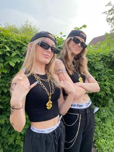 two women in black outfits with tattoos on their arms and one pointing at the camera