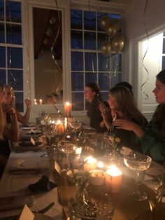 a group of people sitting at a table with candles in front of them and balloons floating from the ceiling