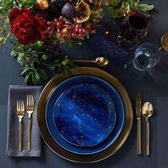 a table setting with blue and gold plates, silverware, flowers and napkins