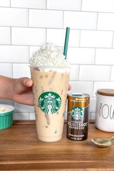 someone holding up a starbucks drink with whipped cream on top and a can of coffee next to it