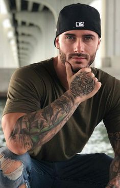 a man with tattoos on his arm sitting next to the water and looking at the camera