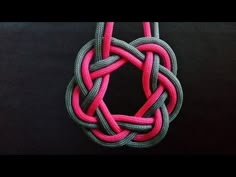 a pink and grey necklace with an intricate knot in the center on a black background