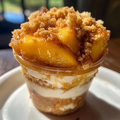 an ice cream sundae with peaches and crumbs in it on a white plate