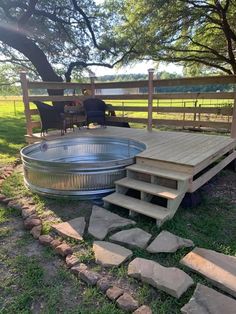 a wooden deck with steps leading up to an outdoor hot tub in the middle of a field