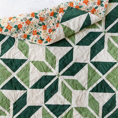 a green and white quilt with an orange flowered design on the top is laying down