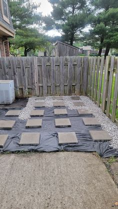 an outdoor area that has been covered with tarp and gravel, in front of a wooden fence