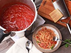 a bowl of spaghetti next to a pot of tomato sauce on a table with bread