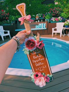 a person holding up a sign next to a swimming pool with flowers on the side