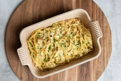 a casserole dish on a wooden platter with cheese and herbs in it