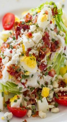 a white plate topped with lettuce and bacon covered in dressing next to tomatoes