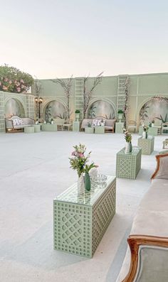 an outdoor seating area with tables and couches in the middle, surrounded by greenery