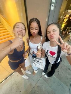 three girls standing on the sidewalk with their fingers in the air and one girl holding an ice cream cone