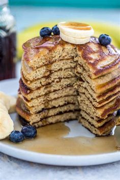 a stack of pancakes with blueberries and bananas on a plate next to some syrup