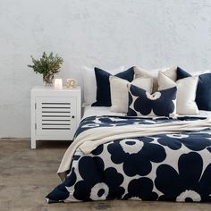 a bed with blue and white flowers on it, next to a night stand in the corner