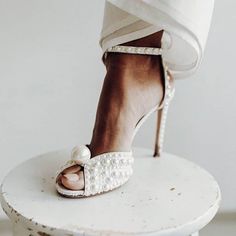 a woman's feet in high heels on top of a white table with pearls