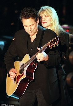 a man holding a guitar while standing next to a woman with blonde hair on stage