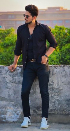 a man in black shirt and jeans leaning against a wall with his hands on his hips