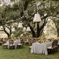 an outdoor dining area with tables, chairs and lamps hanging from the trees in front of them