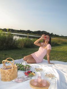 a woman sitting on a blanket in front of a picnic table with food and drinks