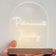 a person holding a wooden block with a light up sign on it that says permanent jewelry