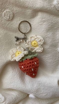 a crocheted strawberry keychain is laying on a white blanket with flowers