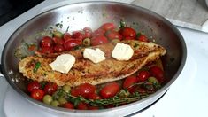 a pan filled with chicken, tomatoes and olives on top of a stovetop