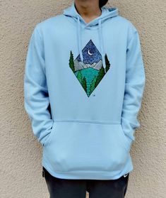 Men’s hoodie with minimal geometric landscape design in the chest area. The design is handpainted and it represents a lake scene with mountains in the background during night time. It’s created in an abstract kind of way and it’s painted with a natural palette of colors. It’s a great gift idea for your loved ones (especially for those who love nature) or for yourself. The hoodie despite the baby blue color shown in the photos, is also available in black. The size scale contains S, M, L and XL.
The hoodie itself has a front pocket and a back hood with strings that fall in the front. It’s made out of cotton and polyester so it’s breathable and comfortable. Geometric Landscape Design, Geometric Landscape, Hoodie Customize, Painting Hoodie, Art Sweatshirt, Lake Scene, Natural Palette, Baby Blue Color, Baby Blue Colour