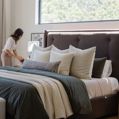 a woman standing next to a bed with pillows and blankets on it in a bedroom