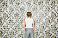 a person standing in front of a wall with a floral pattern on it's walls