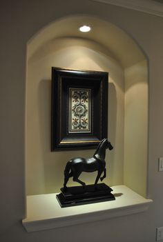 a black horse statue sitting on top of a white shelf next to a framed painting