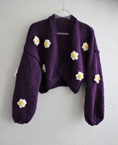 a purple sweater with white flowers on it hanging from a hook against a wall,