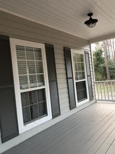 a porch with shutters and two windows on the side of it, next to a light fixture