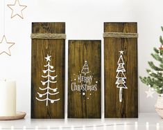 three wooden christmas signs on a table next to a lit candle and a small tree