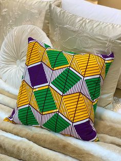 a colorful pillow sitting on top of a bed next to white sheets and pillows in a room