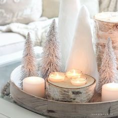 candles are lit on a tray with snow covered trees in front of the couches