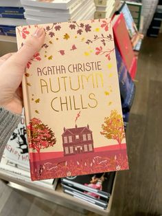 a person holding up a book in front of bookshelves with fall leaves on them