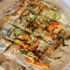 a pizza covered in plastic sitting on top of a wooden cutting board