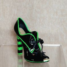 a pair of black and green high heeled shoes sitting on top of a clear shelf