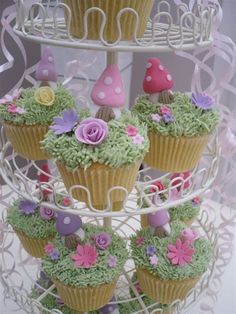 cupcakes decorated with flowers and mushrooms are stacked on a cake stand for display